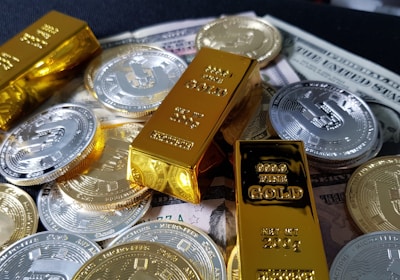 Several gold bars are placed on top of a pile of bitcoin coins and US dollar bills, indicating a scene of wealth and finance.