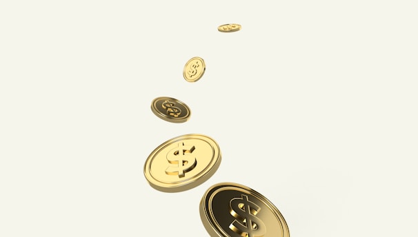 A sequence of golden coins with dollar signs is floating or falling diagonally across a light background. The coins appear shiny and metallic, suggesting wealth or financial growth.